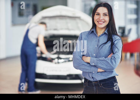 Woman at a car garage getting mechanical service. The mechanic works under the hood of the car Stock Photo