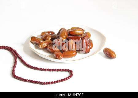 Closeup of porcelain plate with date fruits and prayer beads on the white table. Greeting card for iftar and Ramadan Kareem holiday. Festive background with food. Stock Photo