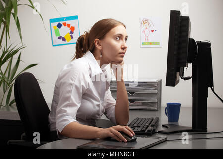Woman woring at computer screen, child's drawing's on the wall in background Stock Photo
