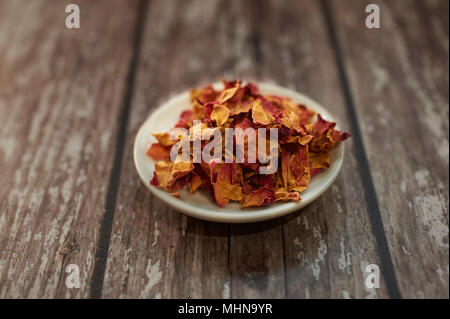 Dry Rose petals in a small white dish on wooden table top Stock Photo