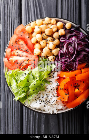 Rice and spicy chickpea vegetable vegetarian buddha bowl. Healthy food concept. On a dark background, vertical top view from above Stock Photo
