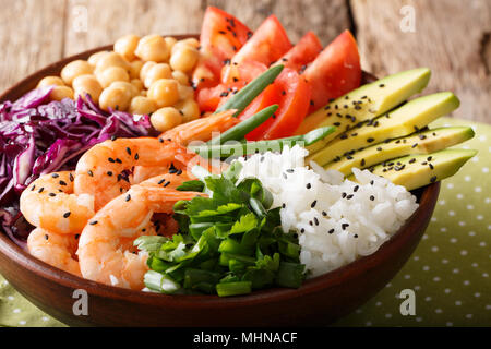 Organic Buddha bowl with prawns, red cabbage, tomatoes, avocado, chickpeas, rice and greens close-up on the table. horizontal Stock Photo