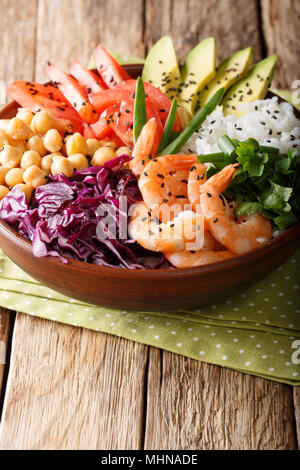 Healthy Buddha bowl with raw vegetables, shrimp, chickpeas, rice and greens close-up on the table. Vertical Stock Photo