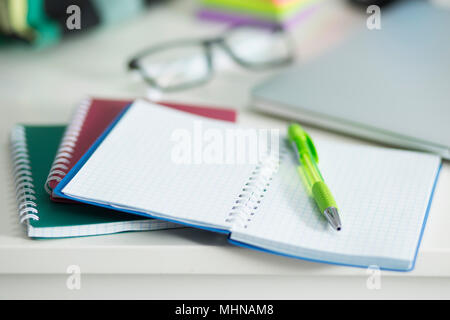 White desktop on which lies an open notebook with a green handle. Nearby is the office and glasses for sight Stock Photo