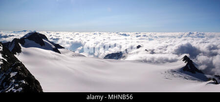 panorama view of a mountain landscape in Switzerland with a large glacier and a sea of clouds below Stock Photo