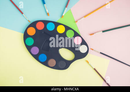 Art palette with paints and paintbrushes on colorful background minimal creative concept. Stock Photo