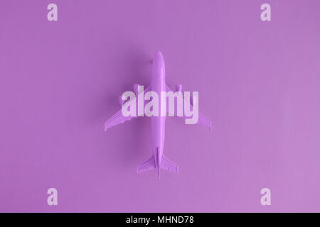 Flat lay of miniature toy airplane on violet background minimal trip and travel creative concepts. Stock Photo