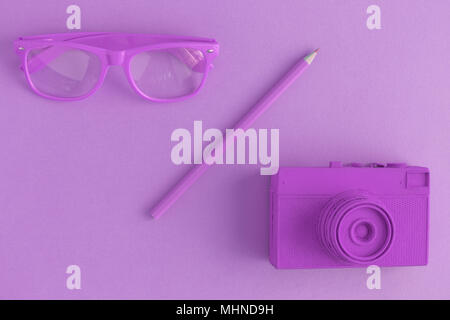 Flat lay of eyeglasses, pencil and retro film photo camera. Purple colored background concept. Stock Photo