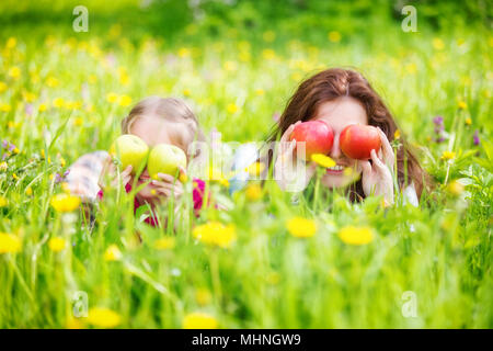 Mother and daughter on sunny meadow with apples in hands Stock Photo