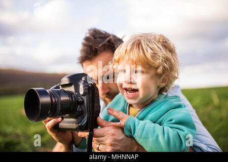 A father and his toddler son with a camera outside in spring nature. Stock Photo