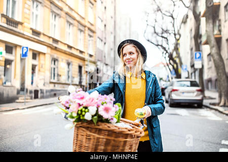 Young woman with bicycle and flowers in sunny spring town. Stock Photo