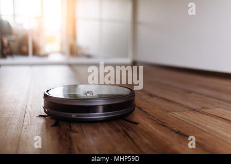 Robotic vacuum cleaner on laminate wood floor smart cleaning technology. Selective focus. Stock Photo