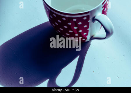 Red coffee mug with white spotted pattern on white table. Above with long shadows Stock Photo