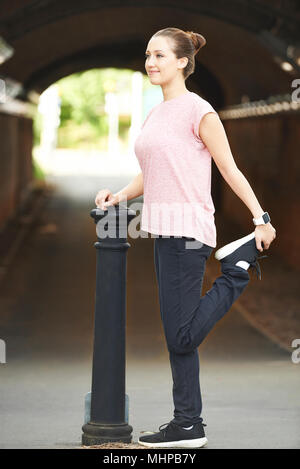 Young Woman Stretching Whilst Exercising In Urban Environment Stock Photo