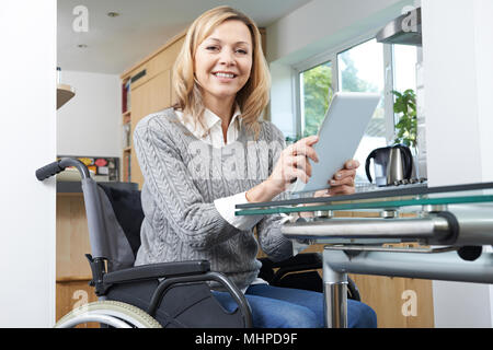 Disabled Woman In Wheelchair Using Digital Tablet At Home Stock Photo