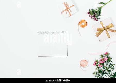 Pink flowers, gift boxes with ribbons and an open blank notebook on a white table top view Stock Photo