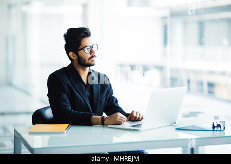 Portrait of busy guy multitasking, taking notes, reading paper, surfing internet with laptop in office Stock Photo