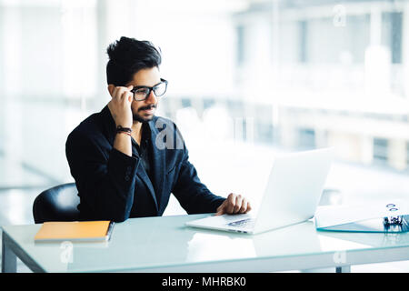 Portrait of busy guy multitasking, taking notes, reading paper, surfing internet with laptop in office Stock Photo