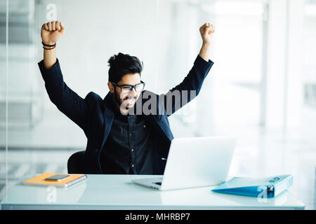 indian young bearded businessman with hands stretched pose while working on laptop celebrating victory mhrbp7