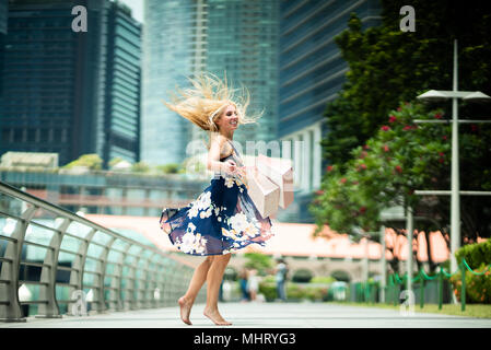The Joy of Shopping... Excited Beautiful Woman  wearing casual blue dress with flowers, shopping bags in the streets with skyscrapers Stock Photo