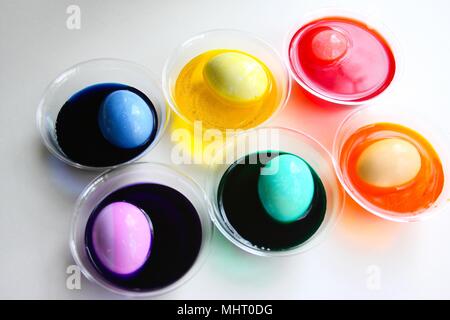 A bright and colorful image of eggs being dyed for Easter. Colored dyes in clear cups with egg in each one, different colors, isolated on white. Stock Photo