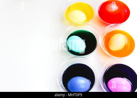 A bright and colorful image of eggs being dyed for Easter. Colored dyes in clear cups with egg in each one, different colors, isolated on white. Stock Photo