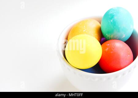 Brightly colored eggs in a white bowl on a white background