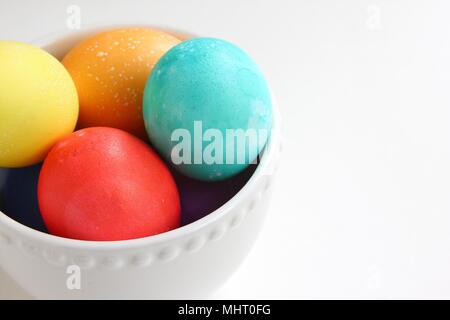 Brightly colored eggs in a white bowl on a white background