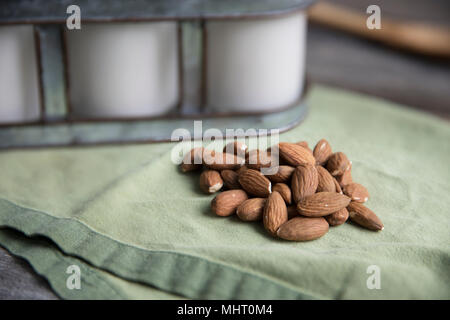 Pile of raw almonds on green napkin with bottles of almond milk in background Stock Photo
