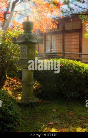 Sun beams over stone pagoda lantern by the pavilion at Japanese Garden during fall season Stock Photo