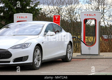 White Tesla Model S electric car connected and charging at Supercharger station on a day of spring in Paimio, Finland - April 28, 2018. Stock Photo