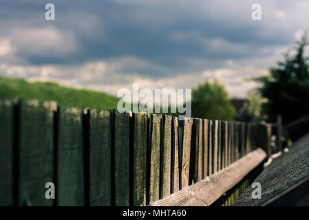 Closeup of a garden fence with heavy dark clouds above it and trees beyond Stock Photo