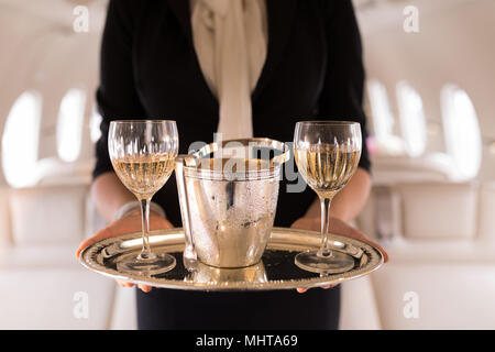 Flight attendant serving glasses of champagne in private jet Stock Photo