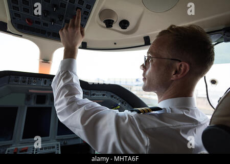 Male pilot pushing button in cockpit Stock Photo