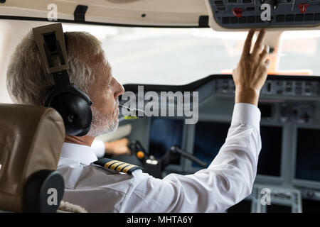 Male pilot pushing button in cockpit Stock Photo