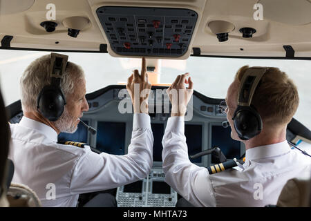 Two male pilots pushing button in cockpit Stock Photo