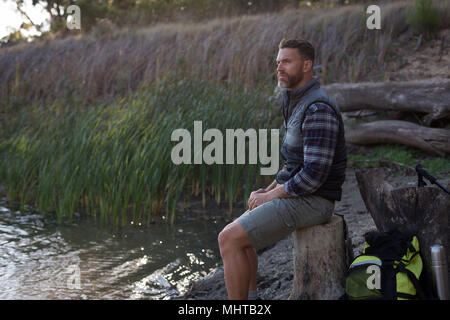 Man relaxing on tree stump near river bank Stock Photo