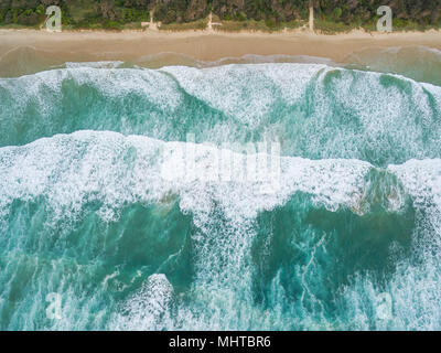 Looking down at large ocean waves breaking on sandy beach