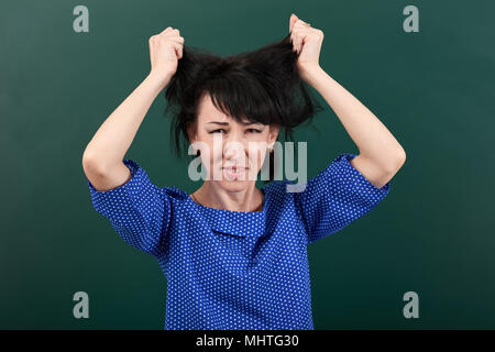 woman teacher in stress posing on chalk board background, touch her hair Stock Photo