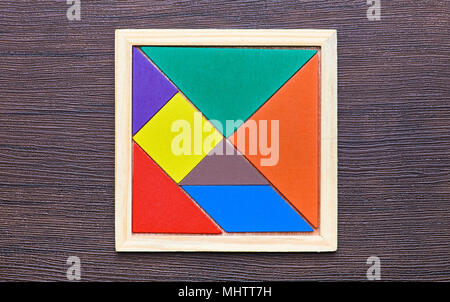 A tangram puzzle consisting of colored pieces with geometric shapes, collected in a square on a dark wooden background Stock Photo