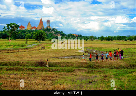 Kanchanaburi, Thailand - July 15, 2011: Group of people walking to work on harvested rice farm on back of Thamsau, Buddhist temple in Kanchanaburi, Th Stock Photo