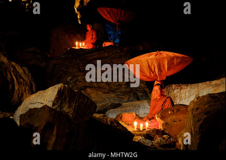 Kanchanaburi, Thailand - July 15, 2011: Buddhist monks sitting with alms bowl, lighten candle and long-handles umbrella to do individual meditation in Stock Photo