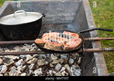 Pieces of red salmon fish grill on a frying pan, which stands on metal rods over the open fire charcoal oven. Preparation of food in a medieval kitche Stock Photo