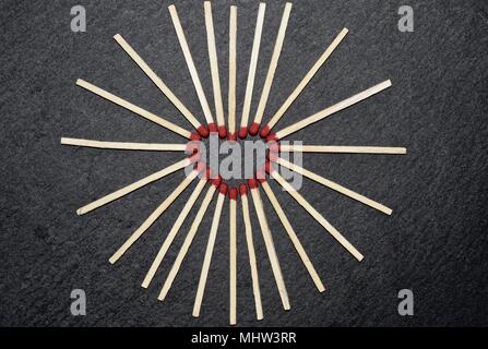 Collection of red head matches laid out in a heart forming shape on a black grey slate background. Stock Photo