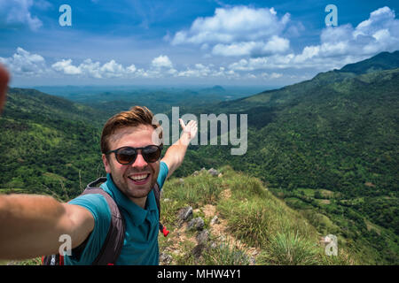 Caucasian man on top of mountain making selfie on background of pretty landscape Stock Photo