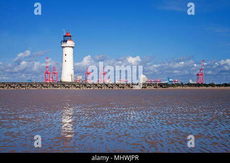 Perch Rock Lighthouse, looking across the sea defences of New Brighton, with the striking red cranes of Liverpool docks in the background Stock Photo