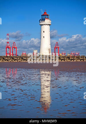 A portrait of Perch Rock Lighthouse, looking across the sea defences of New Brighton, with the red cranes of Liverpool docks in the background Stock Photo