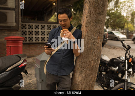 Businessman using mobile phone while eating food Stock Photo