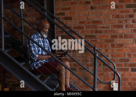 Senior man using laptop on staircase Stock Photo