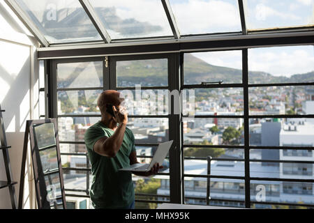 Senior man using laptop while talking on mobile phone Stock Photo